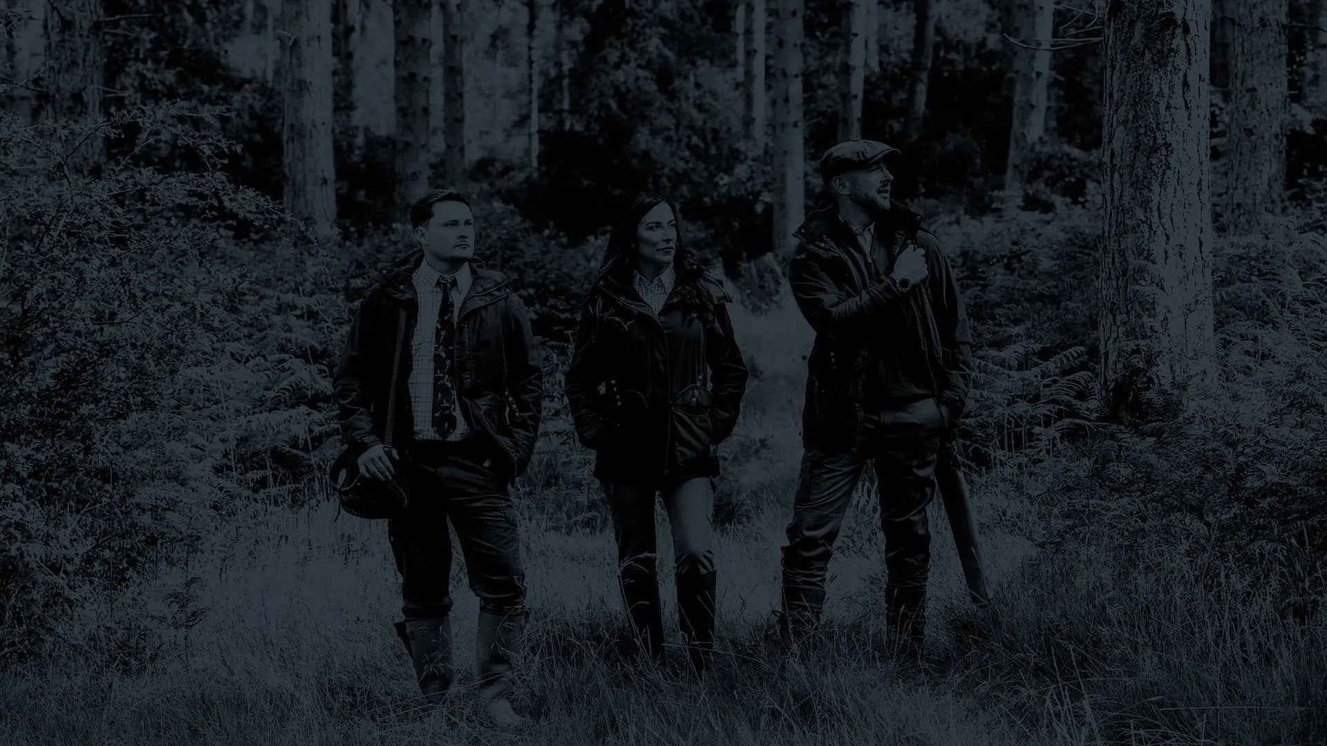 Three folks in rugged forest clothing stand in dim woods for Black Friday.