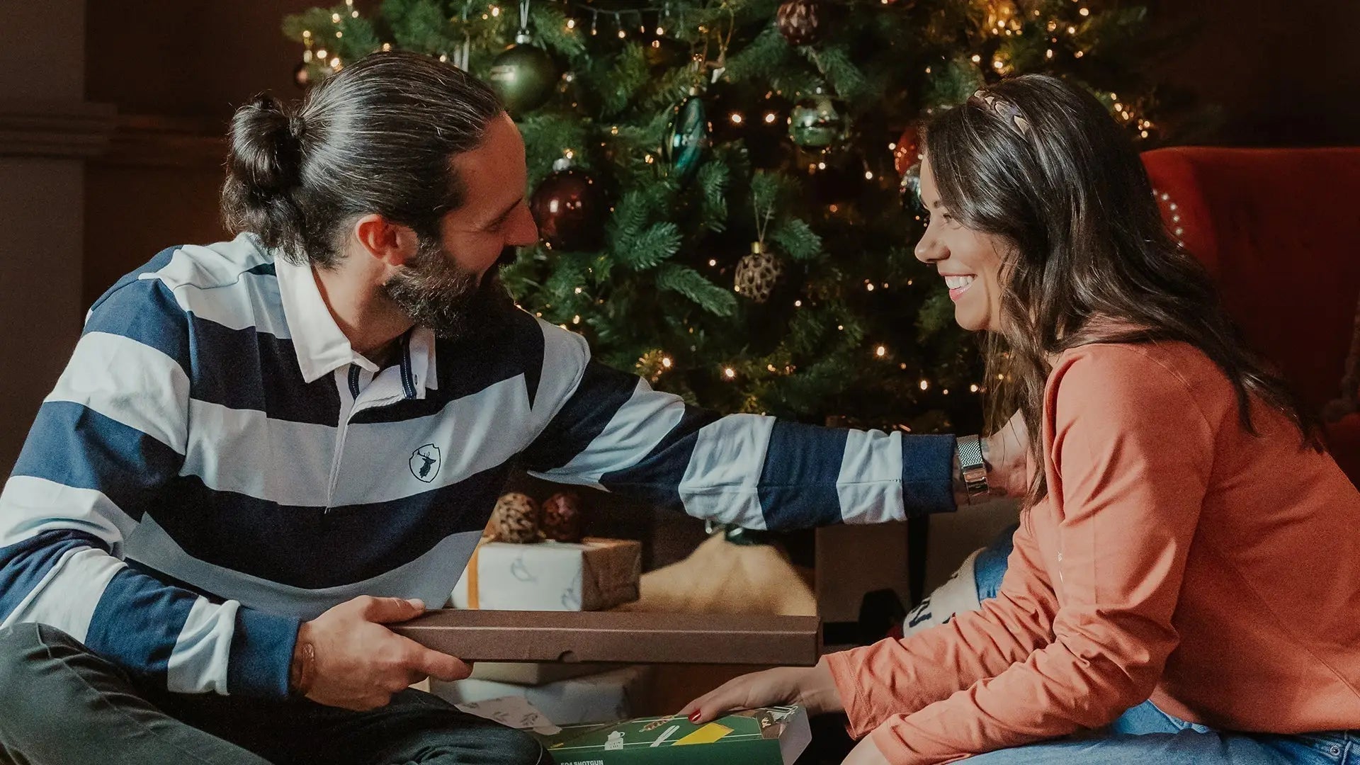 Man in rugby shirt gives Christmas gift to smiling woman at New Forest Clothing