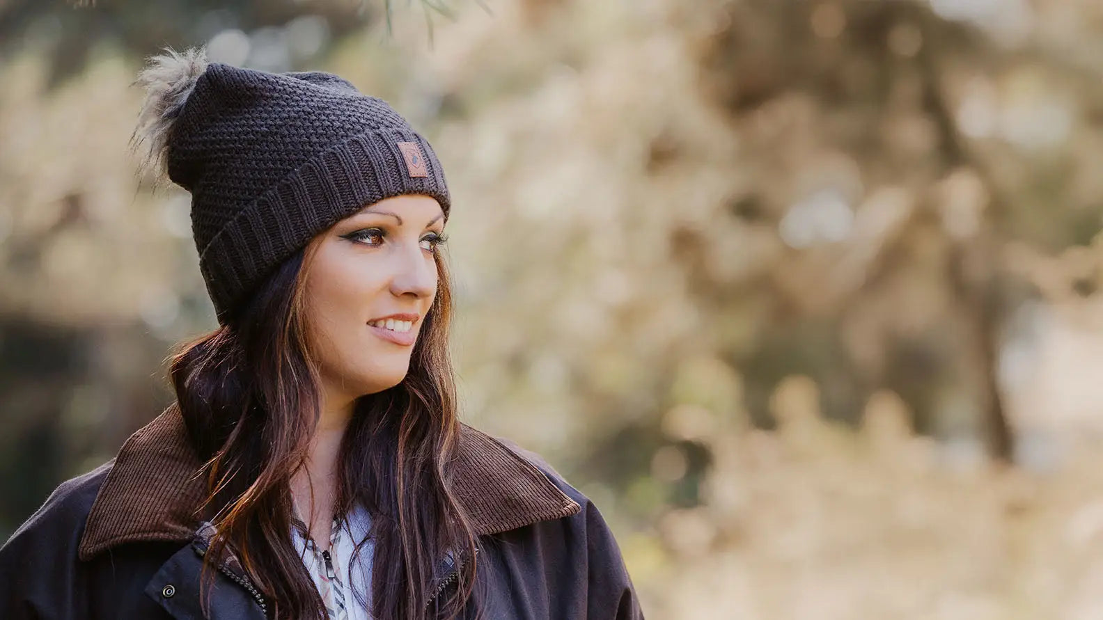Dark gray knit beanie with fluffy pom-pom and brown patch for forest clothing fans