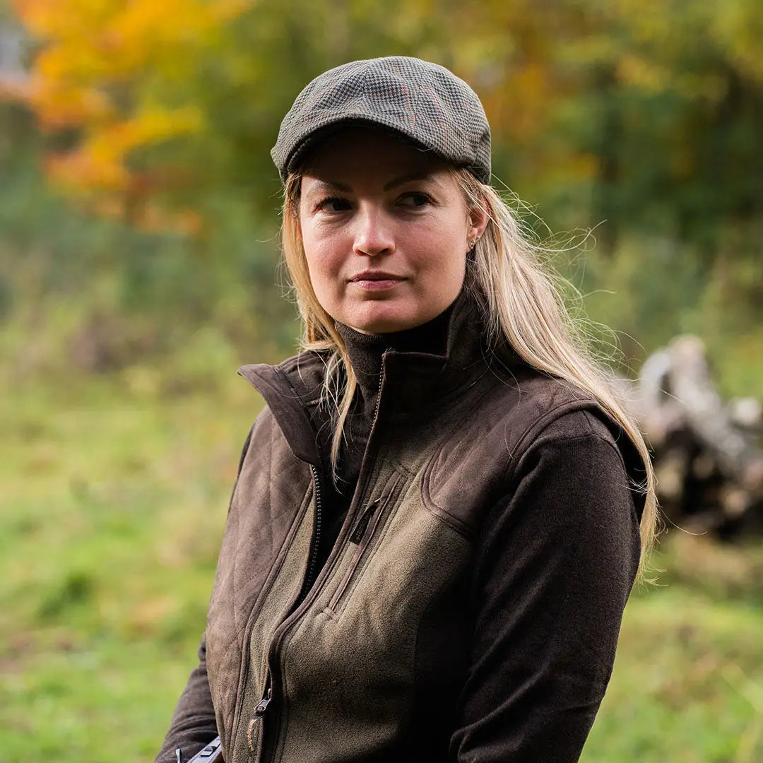 Woman in a tweed cap and vest, showcasing the Deerhunter Pro Gamekeeper Flatcap for hunting