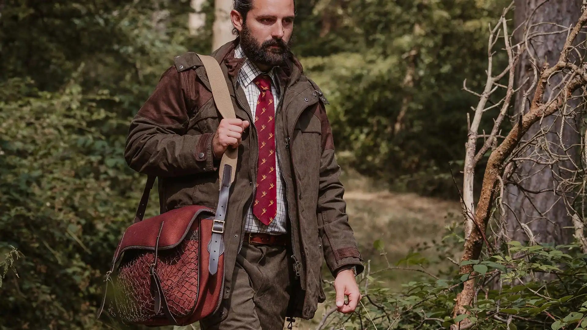 A man in hunting attire carrying a leather shoulder bag.