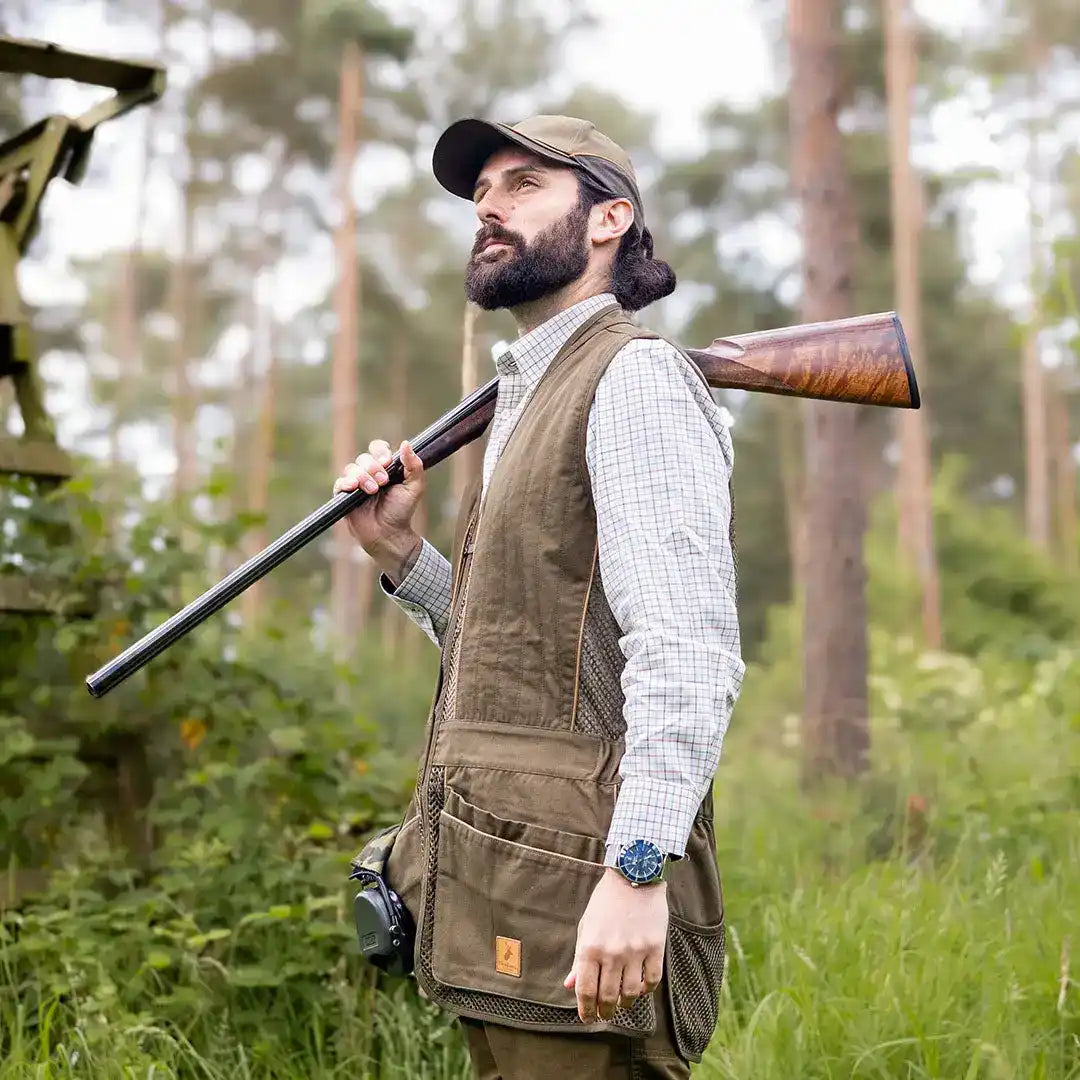 Man aiming a shotgun in the forest wearing a stylish Forest Skeet Vest