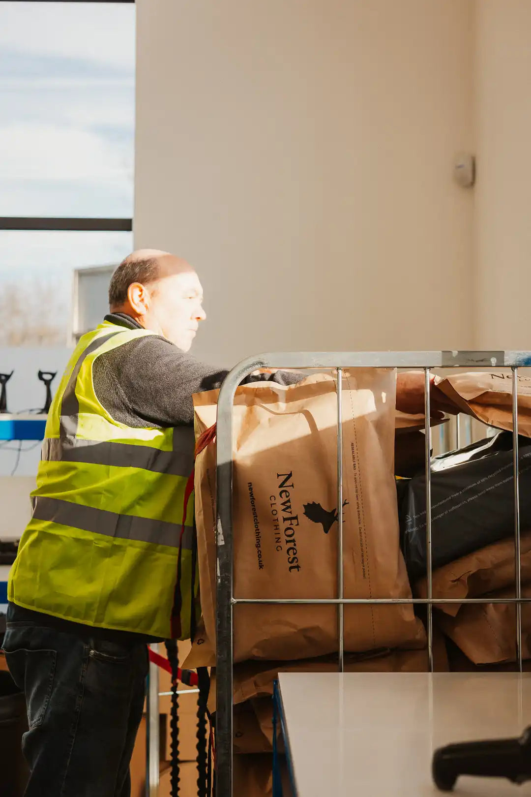 A man in a high-visibility vest leaning on a metal cage filled with brown paper bags.