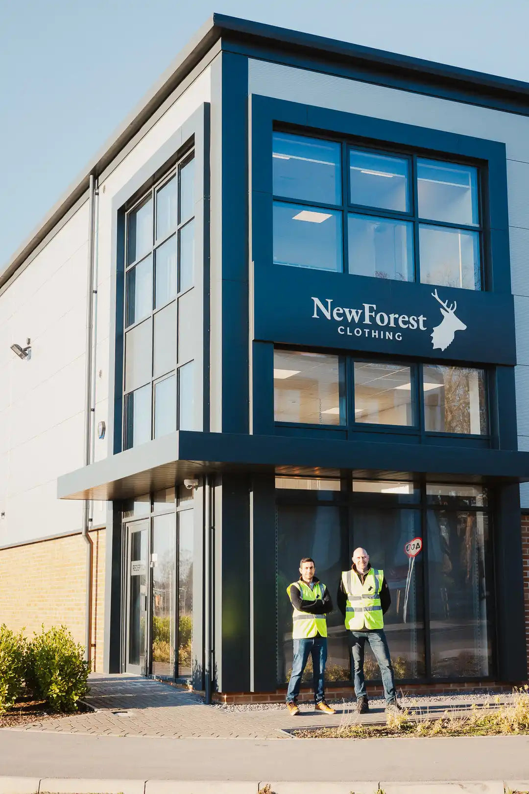 Modern commercial building with two men in high-visibility vests standing outside.