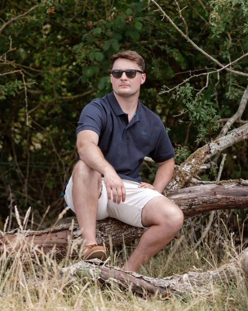 Man in sunglasses sitting on a log wearing the New Forest Pique Polo Shirt in forest pique style