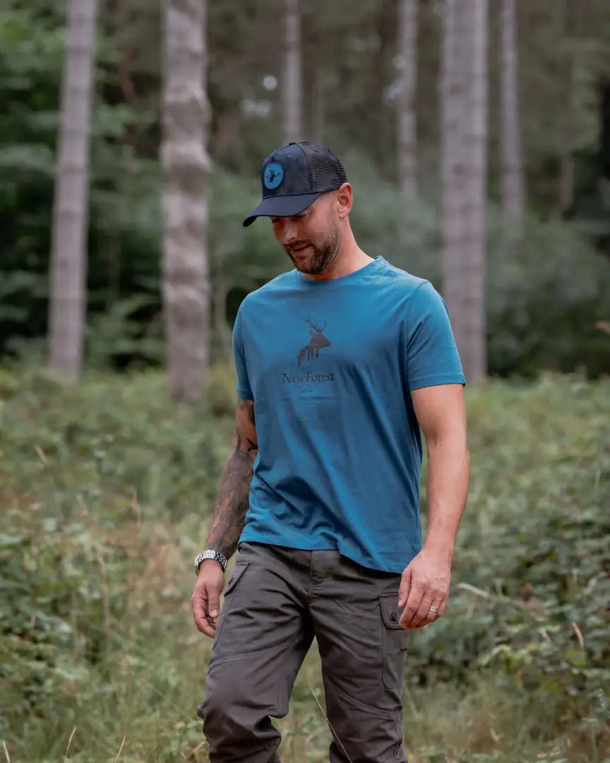 Man in blue T-shirt and cargo pants wearing a new forest trucker hat with rugged charm