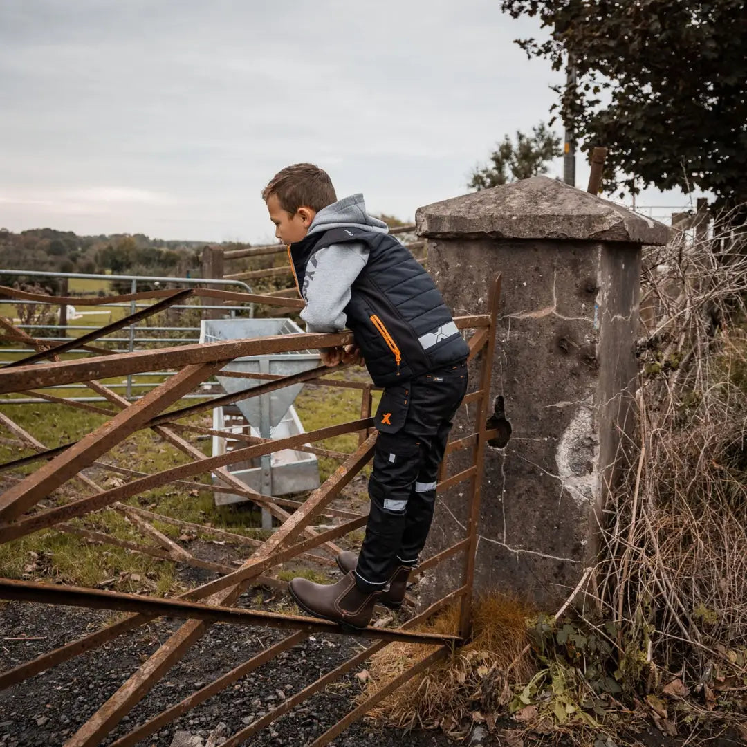 Boy in Xpert Pro Junior Stretch Work Trouser leaning on rusty gate for durable workwear
