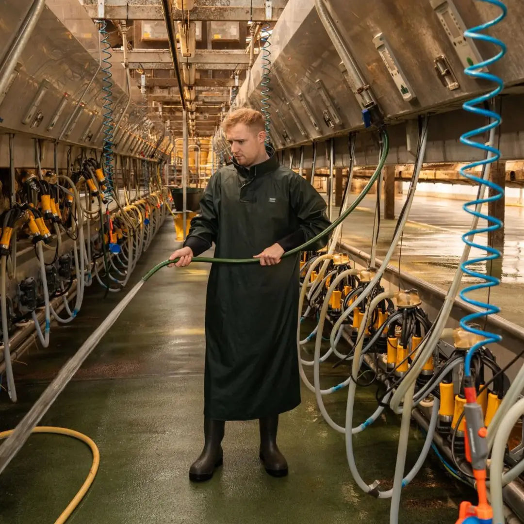 Person in Xpert Swampmaster dairy gown cleaning milking parlor with hose in country clothing