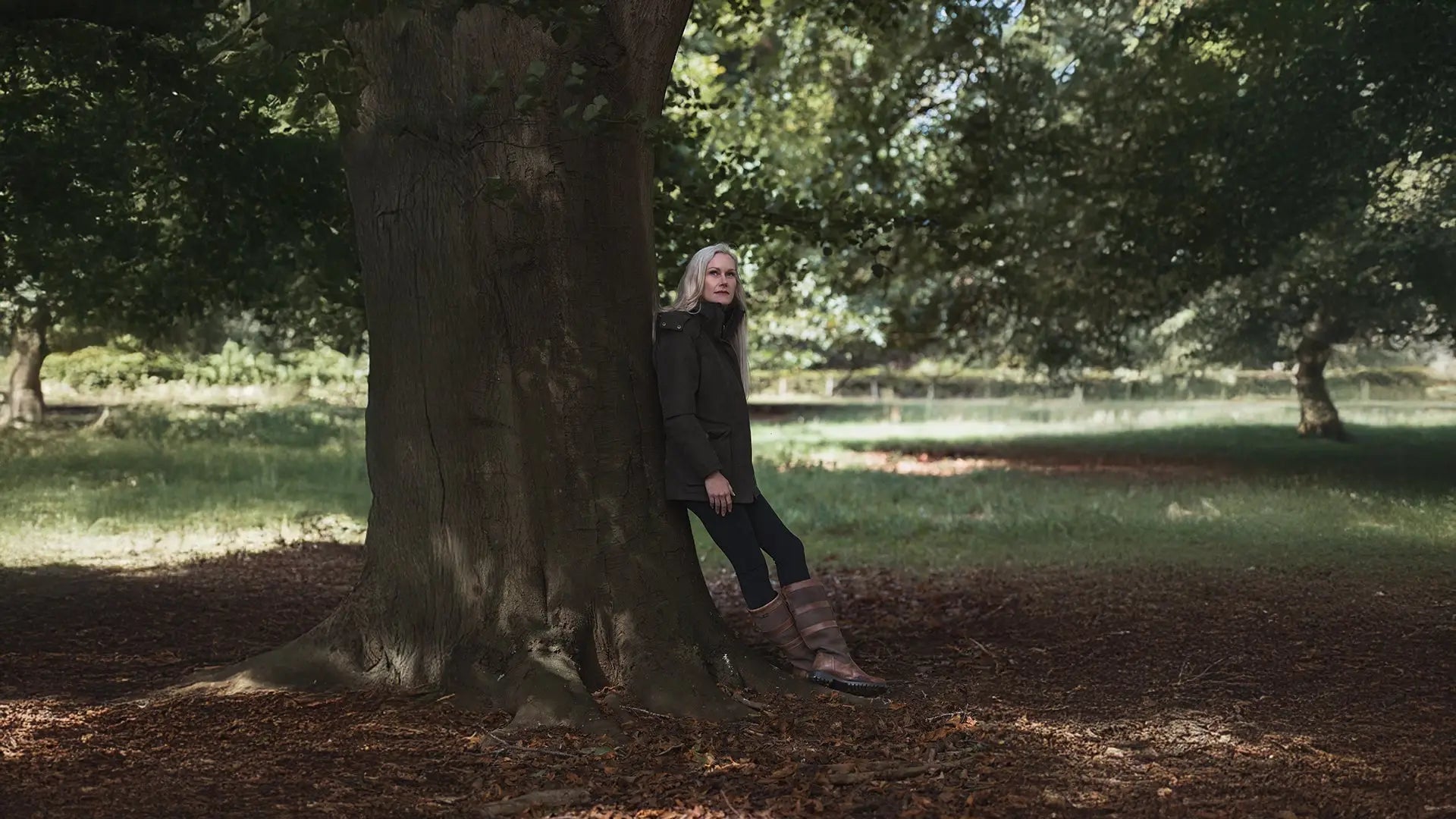 Jessica with long gray hair leans against a tree on shoot day in the field