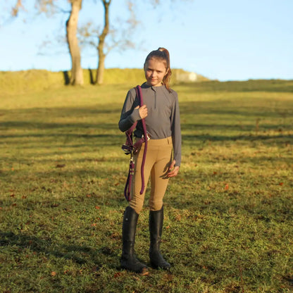 Young girl in equestrian country clothing holding bridle and lead rope outdoors