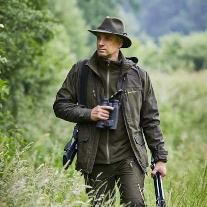 Man in a Deerhunter Chasse Jacket with binoculars walking through tall grass