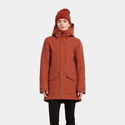 Woman in rust-colored sporty mid-length parka with hood and beanie for Didriksons Frida Womens Parka 7