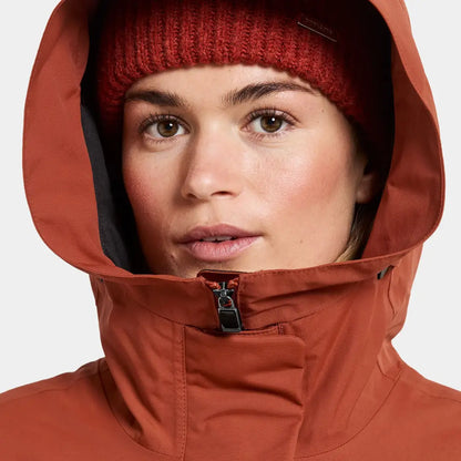 Woman in rust waterproof jacket with hood and beanie, sporty mid-length parka style