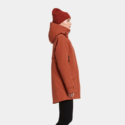 Woman in rust-colored sporty mid-length parka and matching knit beanie for Didriksons Frida Womens Parka 7