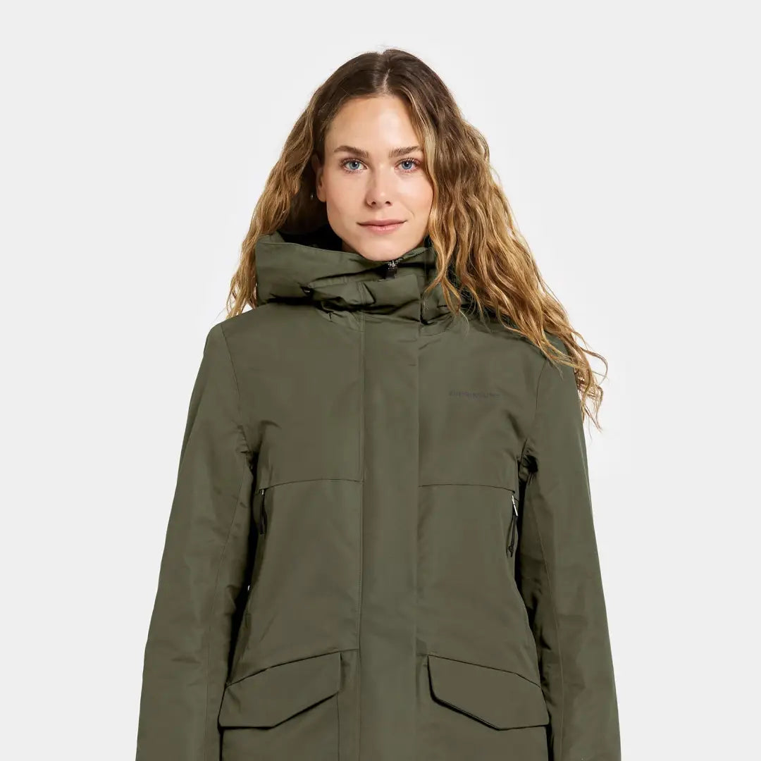 Woman in dark green sporty mid-length parka with hood and front flap pockets