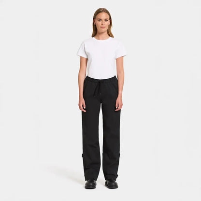 Woman in a white t-shirt and black pants showcasing Didriksons Grit functional rain pants