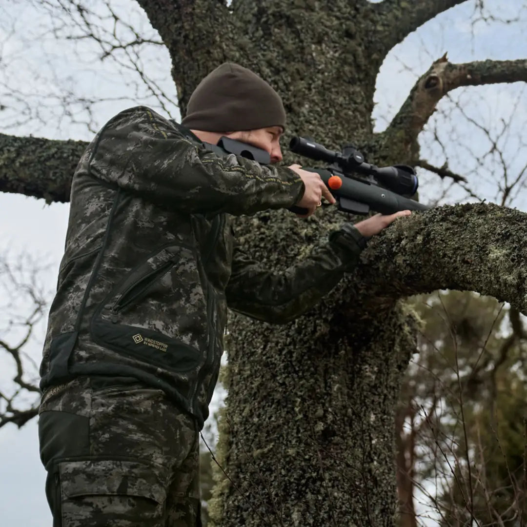 Camouflaged hunter aiming rifle from tree in Härkila Kamko NOCTYX WSP jacket
