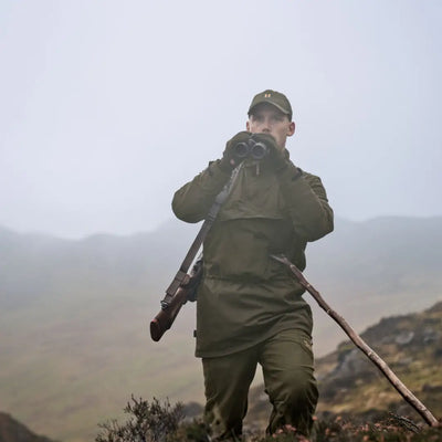 Hunter with binoculars and rifle wearing Härkila Orton Tech packable smock, ideal for country clothing