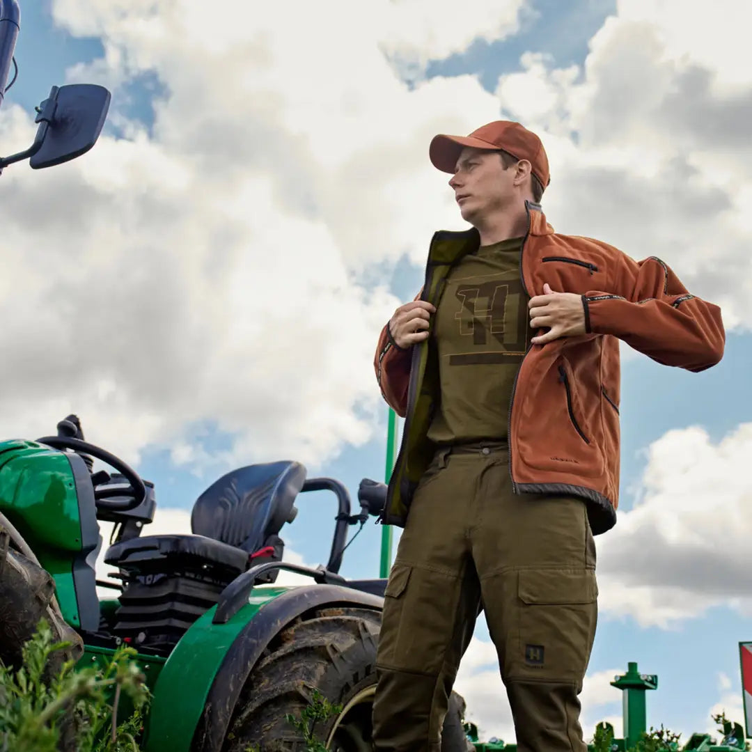 Man in outdoor gear near tractor wearing Härkila Scandinavian Trousers outdoors