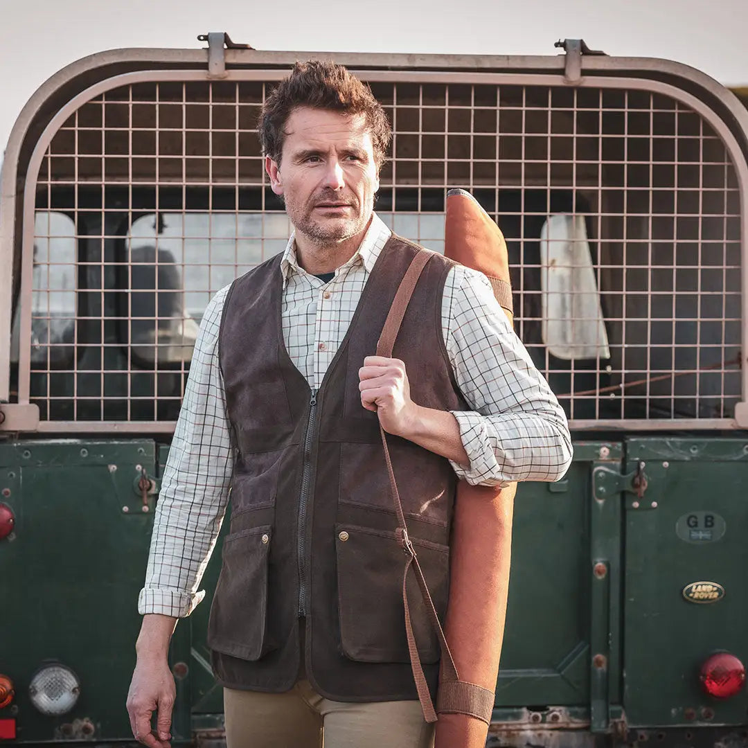 Man in plaid shirt and vest holding rifle case, showcasing Hoggs Of Fife Balmoral Luxury Tattersall Shirt