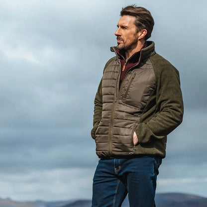 Man in green Melville Hybrid Jacket and blue jeans under an overcast sky