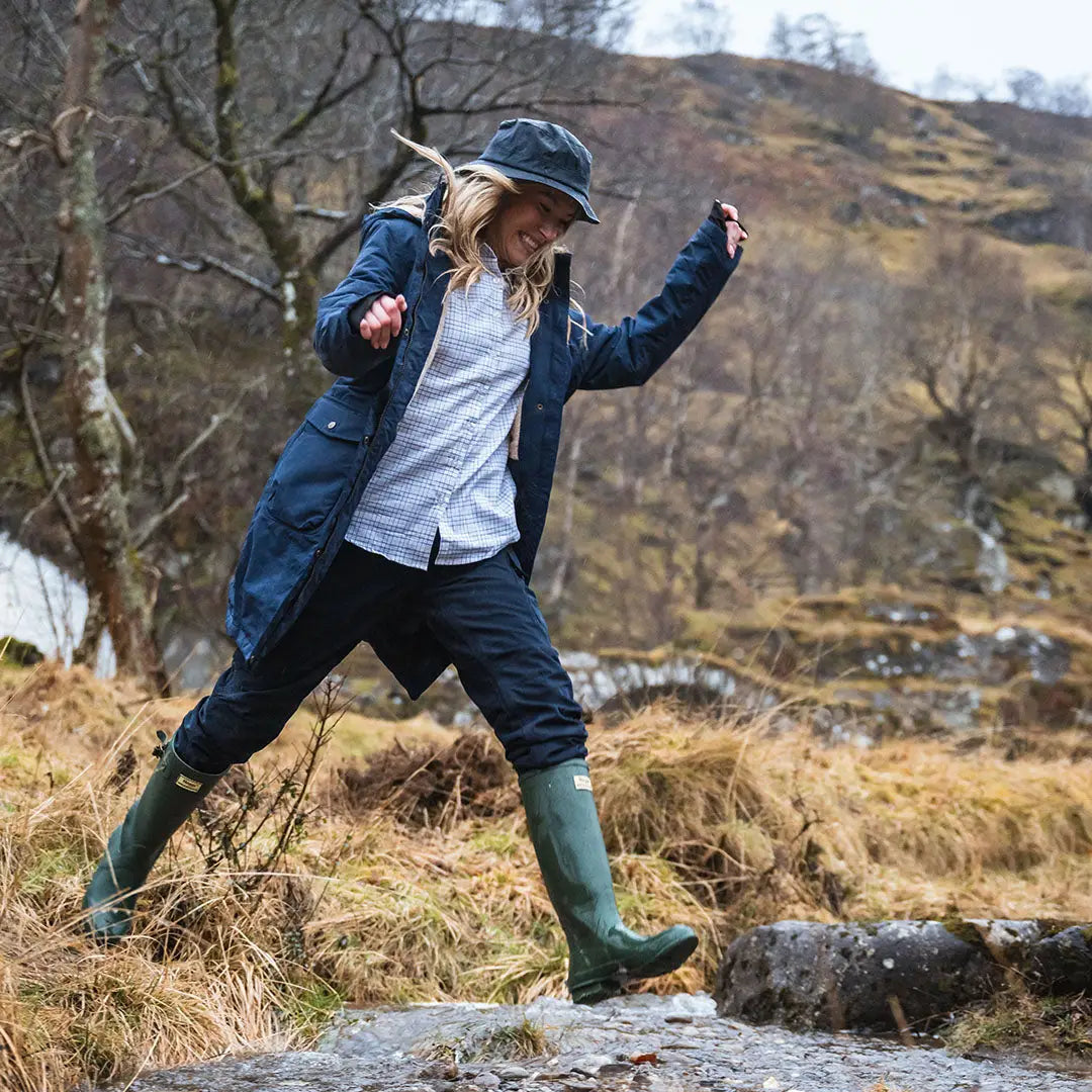 Woman in outdoor clothing joyfully jumping in her Hoggs of Fife Walker Ladies Long Coat