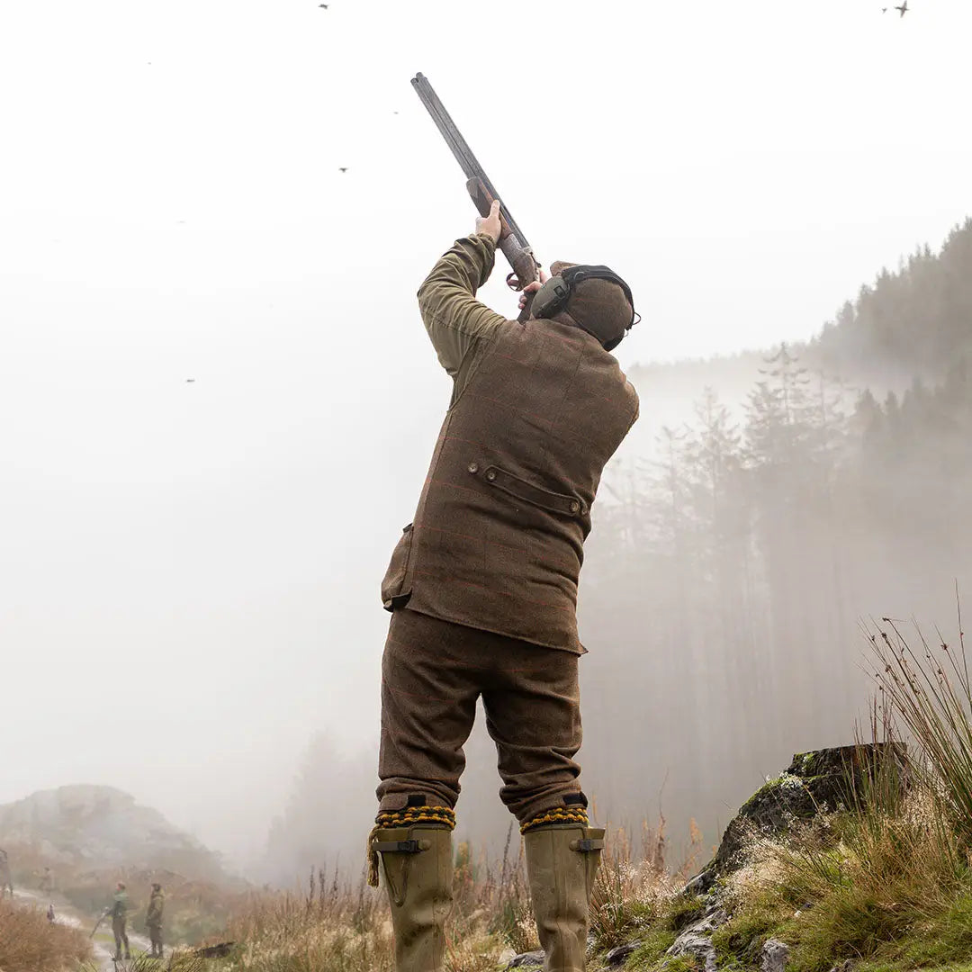 Hunter in Jack Pyke shooting vest aims shotgun in misty sky