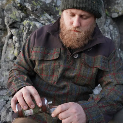 Bearded man in cap pouring liquid, showcasing Harris Tweed Smock style and quality
