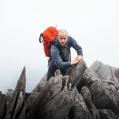 Hiker in a Keela Hydron Softshell Jacket climbing rocky terrain in foggy weather