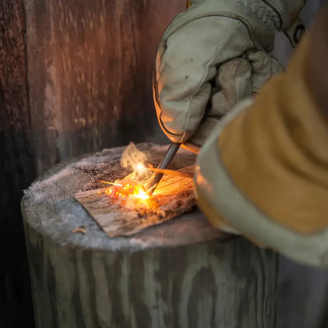 Gloved hands using Kupilka Firesteel compact striker to ignite tinder outdoors
