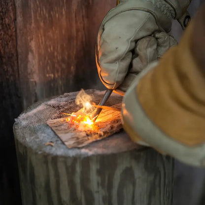 Gloved hands using Kupilka Firesteel compact striker to ignite tinder outdoors