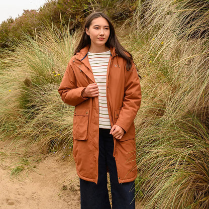 Young woman wearing Lighthouse Imogen Ladies Coat in rust over striped top and dark pants