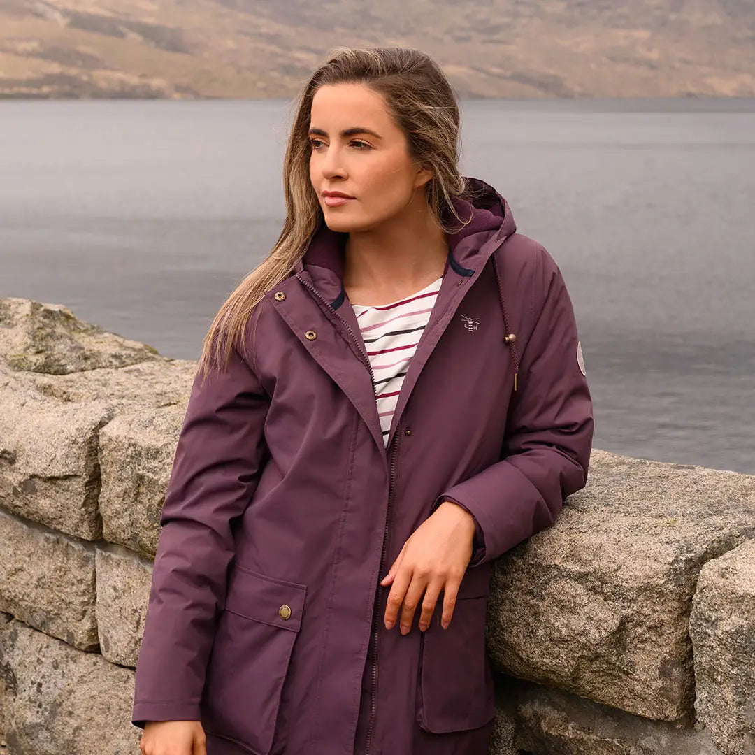 Woman in purple Lighthouse Imogen Ladies Coat leaning on stone wall outdoors