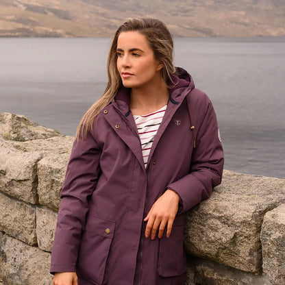 Woman in purple Lighthouse Imogen Ladies Coat leaning on stone wall outdoors