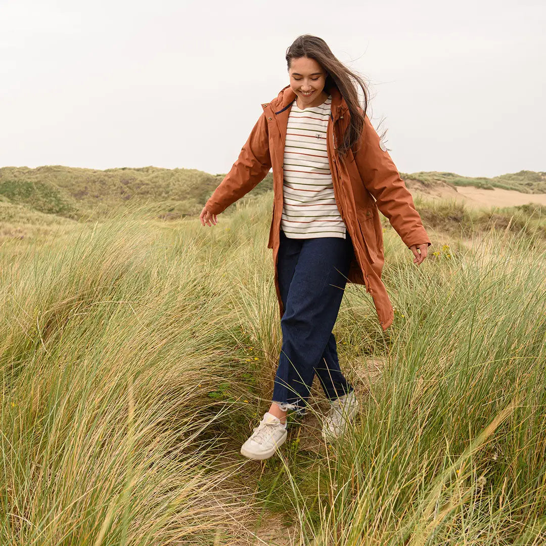 Woman in rust jacket and striped top walking through grass wearing Lighthouse Imogen Ladies Coat