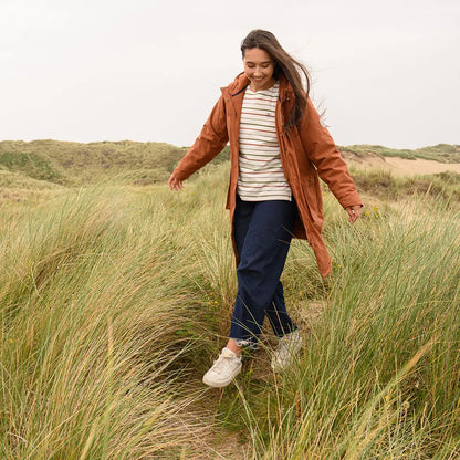Woman in rust jacket and striped top walking through grass wearing Lighthouse Imogen Ladies Coat