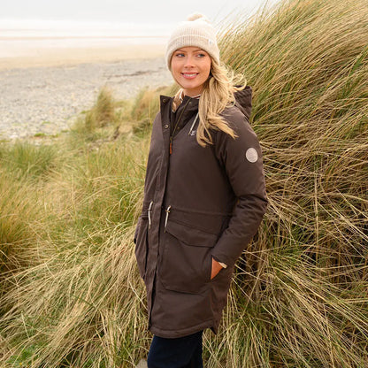 Woman in brown Lighthouse Isobel Coat and cream beanie outdoors near tall grass