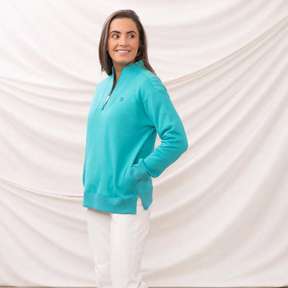 Woman wearing Lighthouse Ladies Coral Jersey turquoise quarter-zip sweatshirt and white pants
