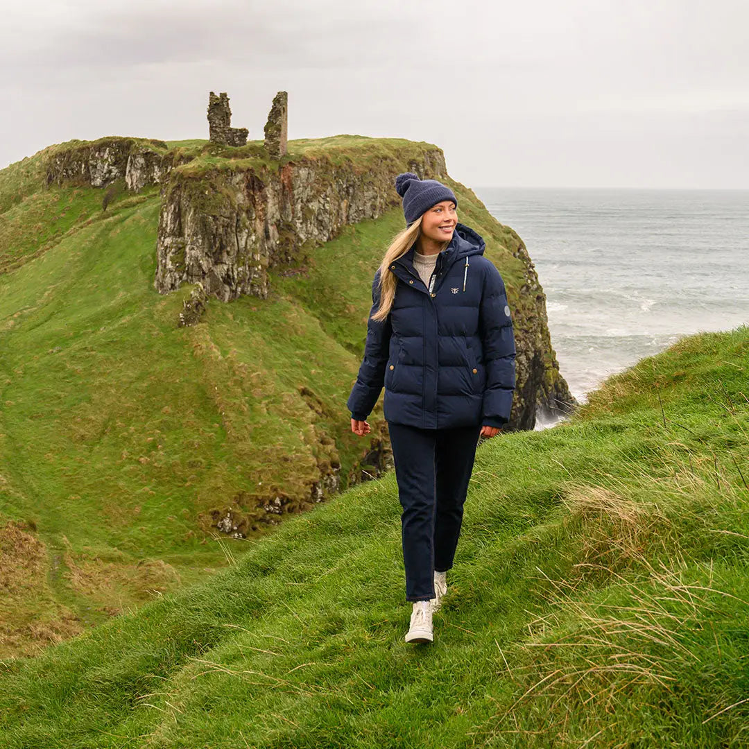 Woman in Lighthouse Margot Ladies Coat walking on grassy hill in dark blue puffer jacket