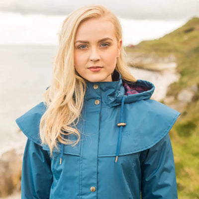 Blonde woman in a teal Lighthouse Outrider waterproof raincoat with a hood