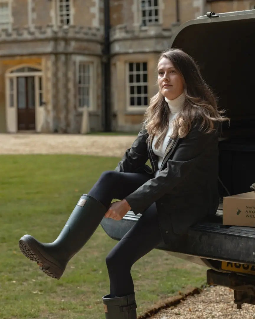 Woman in white turtleneck and black jacket puts on Forest Avon zip Wellington boots