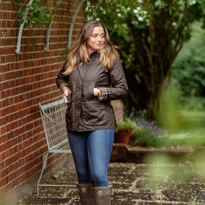 Woman in a brown Forest Freya Ladies Wax Jacket, jeans, and tall boots outdoors