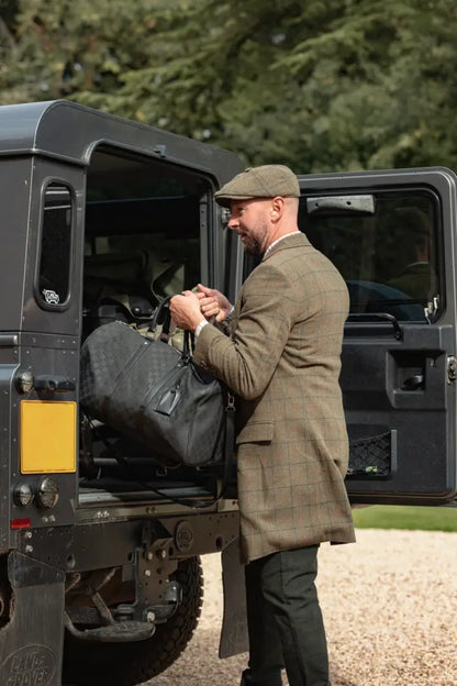 Man in Forest Goodwood Tweed Long Coat loading duffel bag into black SUV