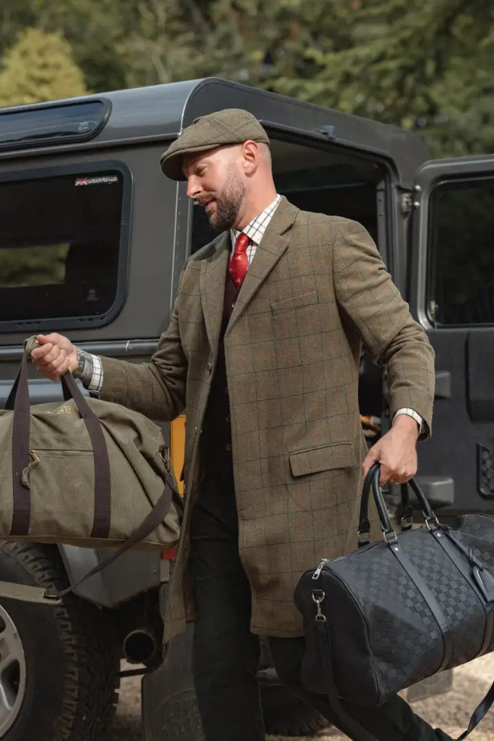 Man in forest goodwood tweed long coat carrying duffel bags outdoors