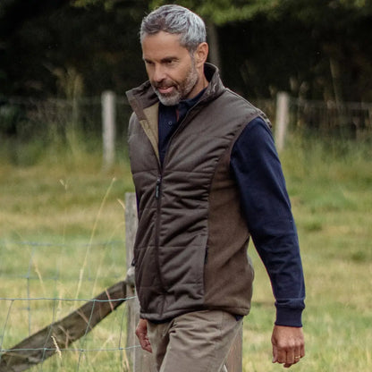 Man with gray hair in a brown vest over a navy sweater, showcasing a stylish Forest Grouse Padded Gilet