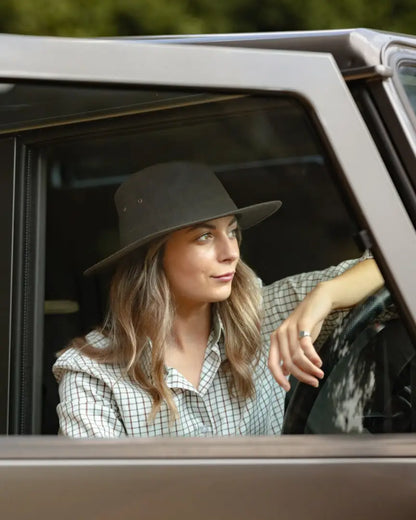Woman in forest harrison waxed hat with wide brim inside a car, checkered shirt style
