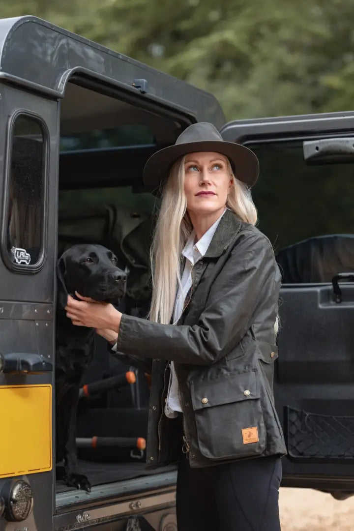 Woman in dark green Forest Harrison waxed jacket with black dog and wide brim Cupra Wax hat