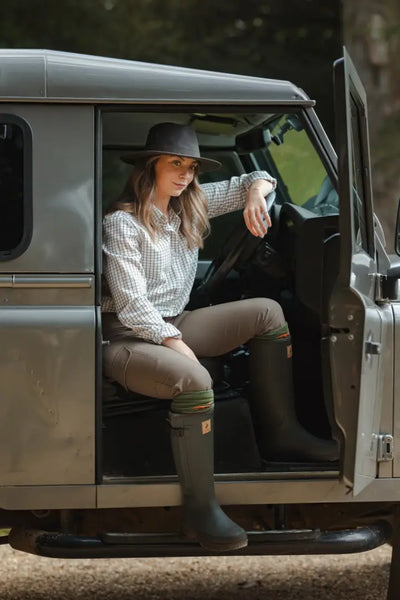 Woman in forest harrison waxed hat and wide brim sitting in Land Rover door open