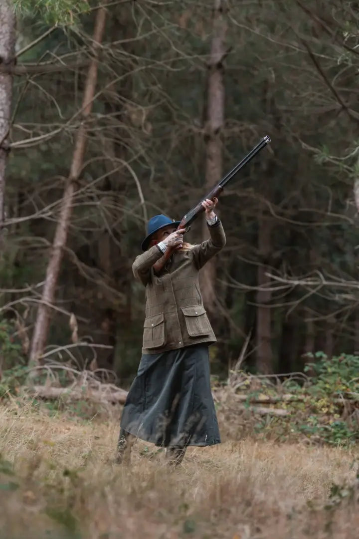 Super stylish ladies field coat in forest, person aiming rifle for hunting adventure