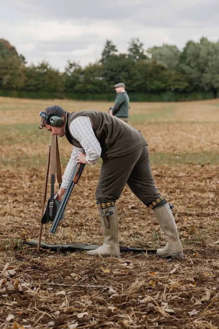 Person in outdoor gear with earmuffs prepping a shotgun wearing Forest Knightwood fleece gilet